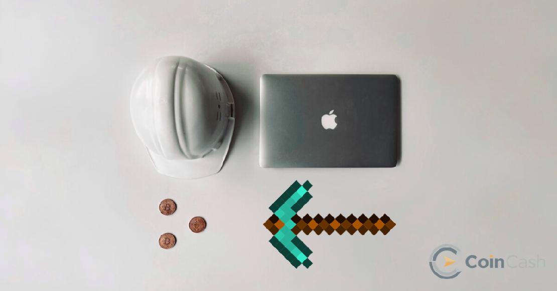 Apple MacBook, kobak, bitcoin érmék és bányász csákány egy fehér asztalon.